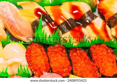 Closeup on Japanese seafood pieces of rice hand-pressed nigirizushi made of anago Congridae with soy sauce, hotate Ezo scallop and gunkanmaki made of ikura red caviar from the roe of salmonid fishes Royalty-Free Stock Photo #2408955421