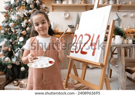 Talented schoolgirl artist paints red numbers 2024 on easel with palette and brush. Christmas tree background. Art school. Happy New Year Eve concept.