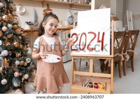 Pretty schoolgirl artist paints red numbers 2024 on easel with palette and brush. Christmas tree background. Art education at school. Merry Christmas and Happy New Year Eve concept.