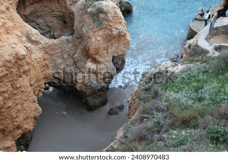 A natural summer beach cave at Praia da Coelha, Algarve, Albufeira. Portugal, vertical photo - Sandstone rock formation on the beach in Algarve, Portugal - Hole of a big cave in the stones