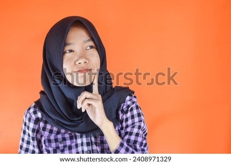 Close Up photo of stunning asian woman in black hijab looking in empty space deep thinking creative person arms on chin wearing purple flannel shirt isolated orange color background