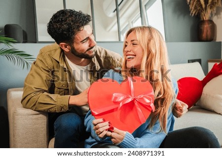 Boyfriend embracing and giving his girlfriend a heart shaped box gift to celebrate Valentines Day. Young couple holding a suprise present on their relationship anniversary. Love and romance date. High Royalty-Free Stock Photo #2408971391