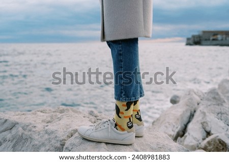 Women legs in sneakers and jeans stand on a stone by the sea. Cropped. Faceless Royalty-Free Stock Photo #2408981883