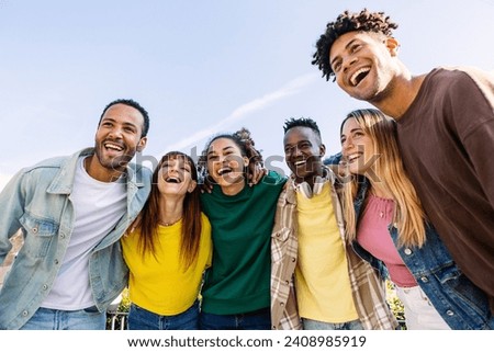 Young group of people having fun together outdoors in a sunny day. Multiracial best friends bonding enjoying time together at city street. United millennial students laughing.