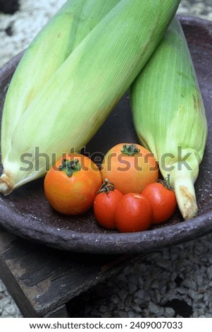Photo of some corn and some tomatoes in a mortar made of clay.