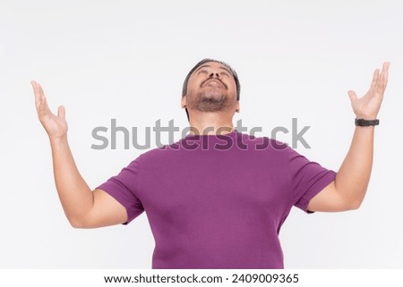 A zealous middle aged man overtly proclaims his faith, raising his hands up and looking up. Wearing a purple waffle shirt, Isolated on a white background.