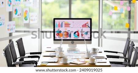 Analysis sales target growth graph chart investment report data on big computer screen monitor placed in middle of meeting table in front glass building windows with garden view in blurred background.