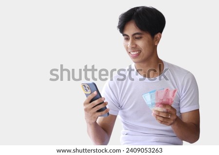 A young handsome man making money from a cellphone app. Holding cash on one hand. Income generation or mobile banking concept.isolated on a White background. Royalty-Free Stock Photo #2409053263