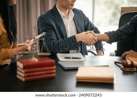 Asian woman yellow top shaking hands with someone across table, while Asian man in suit observes. Legal scales and books visible. legal, legislation Royalty-Free Stock Photo #2409072243