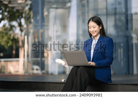 Young Asian business woman leader entrepreneur, professional manager holding digital tablet computer uon the street in big city on business center background. Royalty-Free Stock Photo #2409093981