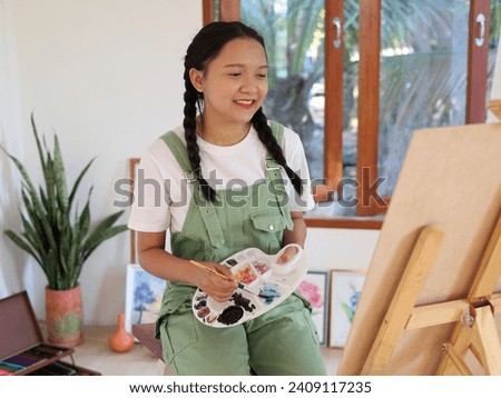 Happy young girl drawing with a paint palette and a paintbrush at home,painting artist.