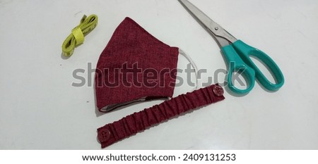 Photo of a three-layer cloth mask. Maroon wolvis fabric. And mask connector strap.
