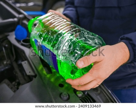 Filling a windshield washer tank with an antifreeze in winter cold weather. The man pours the detergent into the car. The driver pours antifreeze into the tank to spray the windshield during. 