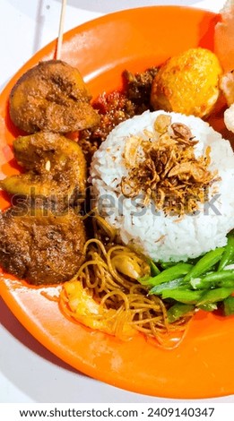 Indonesian food dish usually called Nasi Lemak Medan or Nasi Uduk Medan which contains uduk rice, boiled chili eggs, green beans, fried vermicelli, jengkol satay, fried onions and crackers.  Royalty-Free Stock Photo #2409140347