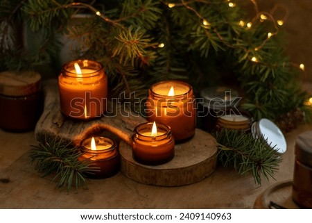 Soy candles burn in glass jars. Comfort at home. Candle in a brown jar. Scent and light. Scented handmade candle. Aroma therapy. Christmas tree and winter mood. Cozy home decor. Festive decoration. Royalty-Free Stock Photo #2409140963