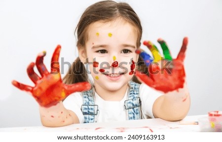 Art drawing for children. A child girl on at table indoors with her hands stained in paint.