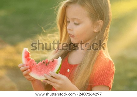 a little girl with long hair in a red dress eats a watermelon on the lawn. picnic in the park. happy childhood. space for text. High quality photo