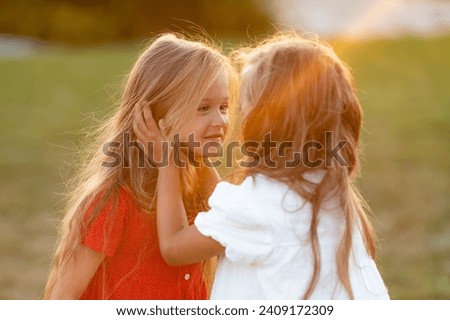Two cute beautiful sisters playing and hugging at sunset outdoor. Spring summer inspiration emotional portrait background