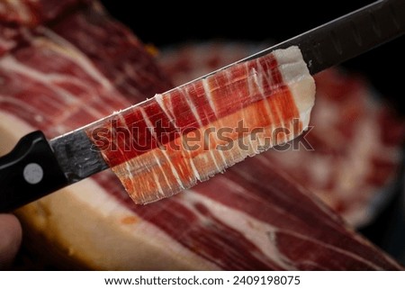 Close up view of a slice of acorn-fed Spanish Iberian pork ham cut with a knife. Iberian ham with selective focus hand cut by professionals for tasting. Royalty-Free Stock Photo #2409198075