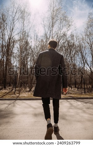 He is wearing a coat and trousers, and is surrounded by trees and a cloudy sky.