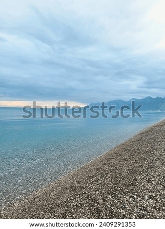This captivating image captures the breathtaking beauty of Konyaaltı Beach in Antalya, Turkey. The foreground features smooth pebbles strewn along the shoreline, bathed in the gentle caress of waves.