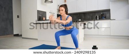 Portrait of young woman doing aerobics exercises in living room, sport training at home, standing on rubber fitness mat and doing workout.