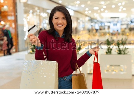 Beautiful woman holding credit card and shopping bags in mall
