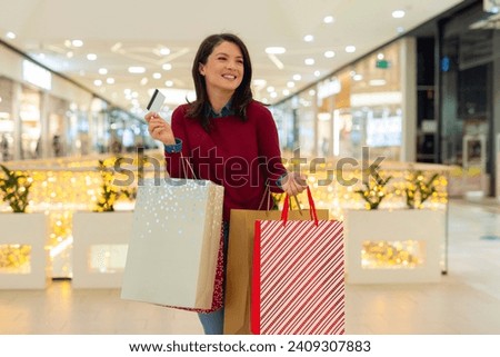 Cute woman holding credit card and shopping bags in mall