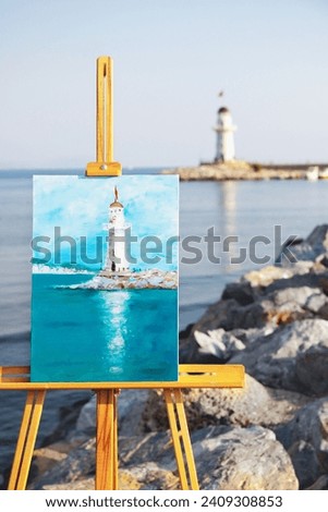 Colorful acrylic painting depicting the white lighthouse in Alanya, Turkiye. Beautiful picture on canvas standing on the wooden easel. Life drawing art concept. Selective focus. Blurred background.