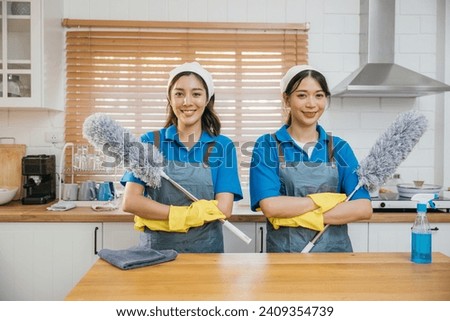 Portrait of two Asian housekeepers on kitchen counter with duster foggy spray and rag. Their teamwork effective housework and hygiene. Clean portrait two uniform maid working smiling employee. Royalty-Free Stock Photo #2409354739