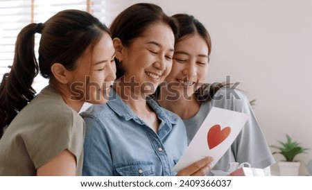 Mother day two grown up child cuddle hug give flower gift box red heart card to mature mum. Love kiss care mom asia middle age adult three people sitting at home sofa happy smile enjoy family time. Royalty-Free Stock Photo #2409366037