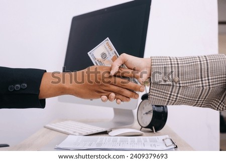Two business people making handshake with money in hands at office. Bribery, corruption and venality concepts Royalty-Free Stock Photo #2409379693