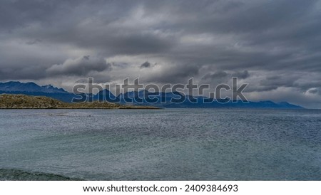 Beautiful seascape of Patagonia. Ripples on the turquoise water of the Beagle Canal. An island with stunted vegetation in the distance. The Andes mountains against a cloudy sky. Argentina. 