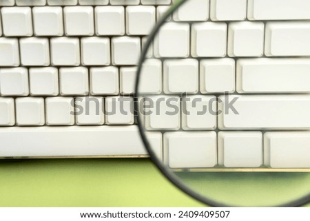 A closeup view of a magnifying glass focuses on a computer keyboard button on a colored background