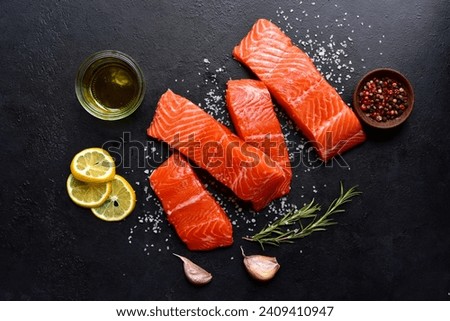 Raw fresh organic trout fillet with ingredients for cookin on a black slate, stone or concrete backgroundg. Top view with copy space.
