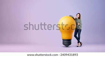 Smiling woman showing thumb up, full length standing near large lightbulb on empty purple background. Concept of support, creativity, plan and business idea