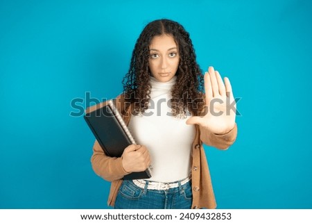Student arab girl with curly hair shows stop sign prohibition symbol keeps palm forward to camera with strict expression