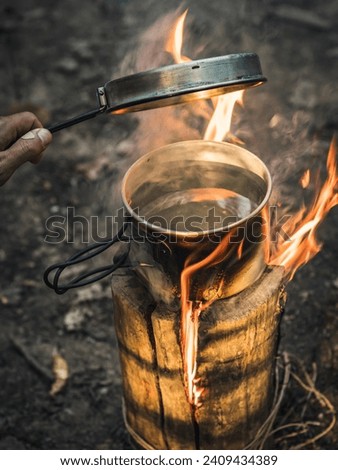 Water boiling in a metal pot on Swedish Fire Log. Burning a Swedish candle, swedish torch in summer evening in a forest with fire and smoke