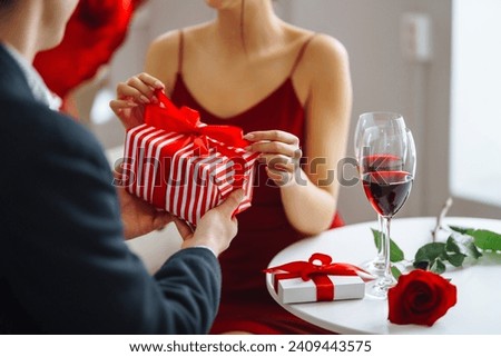 Young couple in love celebrates Valentine's Day. A man and a woman are enjoying time together in a restaurant, giving gifts, relaxing. Concept of romance, love. Royalty-Free Stock Photo #2409443575