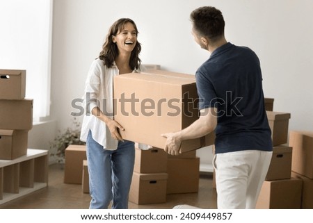 Cheerful young husband and wife moving into new house, flat, carrying cardboard boxes into empty room, smiling, laughing, having fun, walking to stacks of transportation containers