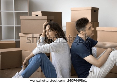 Sad tired married couple moving out from common flat, house, sitting back to back at stack of relocation boxes, looking away, keeping ignoring, thinking on divorce, finance problems, mortgage default Royalty-Free Stock Photo #2409449861
