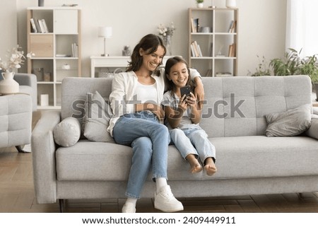 Happy young mother and cheerful daughter kid using online application on mobile phone together for communication, leisure, having fun, taking home family selfie, talking on video call