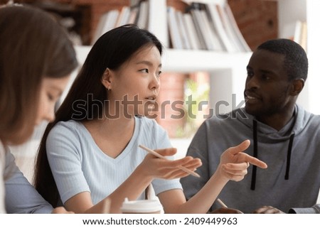 Concentrated Asian female group leader speak on team meeting with multiethnic teammates, international diverse millennial students cooperating in classroom discuss project studying together Royalty-Free Stock Photo #2409449963