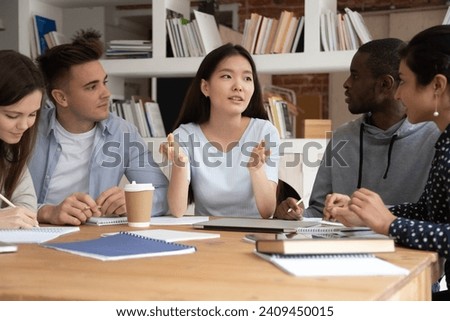 Focused international students sit at desk discuss school educational project brainstorm together, concentrated multiethnic young people study at shared table consider work on paperwork in classroom Royalty-Free Stock Photo #2409450015