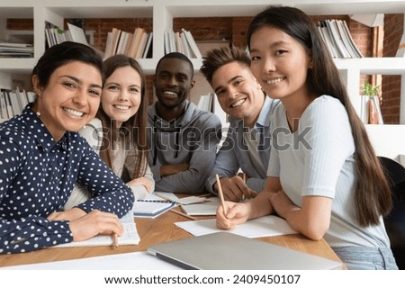 Smiling multiethnic students sit at desk working studying in classroom posing for group picture together, portrait of positive motivated multiracial young people teammates cooperating at lesson