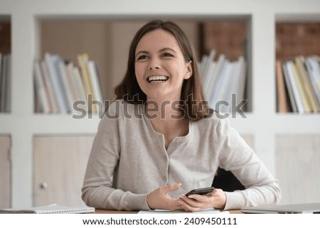 Happy Caucasian millennial girl sit at desk using smartphone look to side talking with teammate in classroom, smiling female student speak chat with group mate, having pleasant conversation Royalty-Free Stock Photo #2409450111