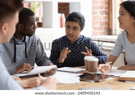 Concentrated multiethnic young people sit at desk studying together discussing group project indoors, focused international diverse students talk share ideas cooperating teamwork in classroom Royalty-Free Stock Photo #2409450143