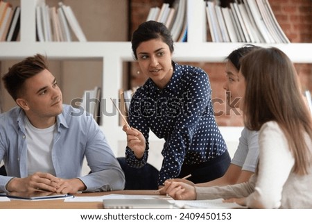 Concentrated multiethnic millennial students gather at desk in classroom discuss school project together, focused multiracial group teammates cooperating brainstorm studying in class, teamwork concept Royalty-Free Stock Photo #2409450153