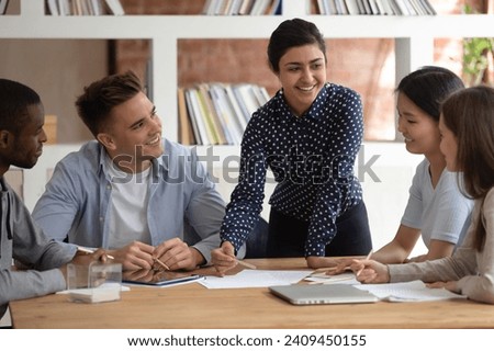Smiling multiracial diverse students sit ta desk in classroom studying together discuss paperwork project, happy multiethnic young people involved in team activity at lesson in class, teamwork concept Royalty-Free Stock Photo #2409450155