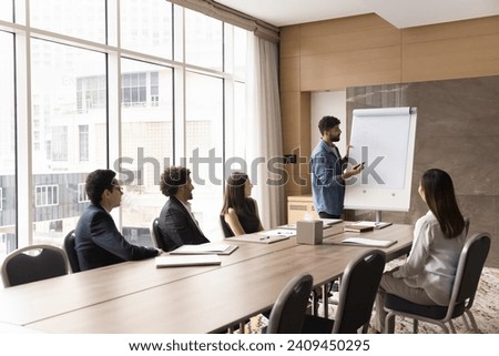 Young Arab project manager presenting marketing plan to team, writing on flipchart, drawing on whiteboard, offering project strategy to colleagues, partners, training employees